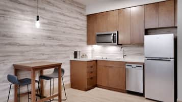A modern kitchen with wooden cabinets, a stainless steel refrigerator, a microwave, a dishwasher, and a table with two chairs.