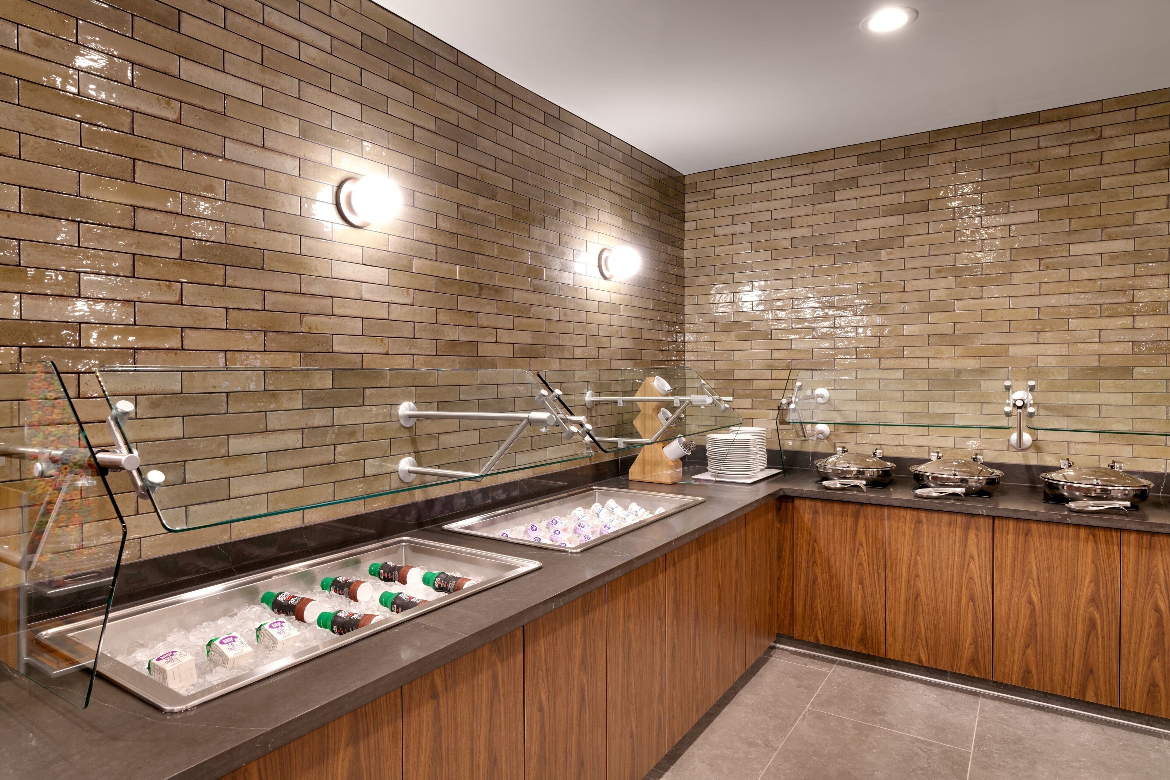 A buffet area with a brick wall, a wooden counter, and various food and drink dispensers.