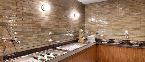 A buffet area with a brick wall, a wooden counter, and various food and drink dispensers.