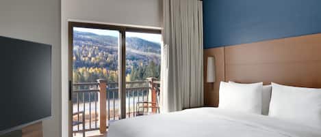 Ein Hotelzimmer mit einem großen Bett, einem Fernseher, einem Balkon mit Bergblick und einer Wand in Blautönen.
