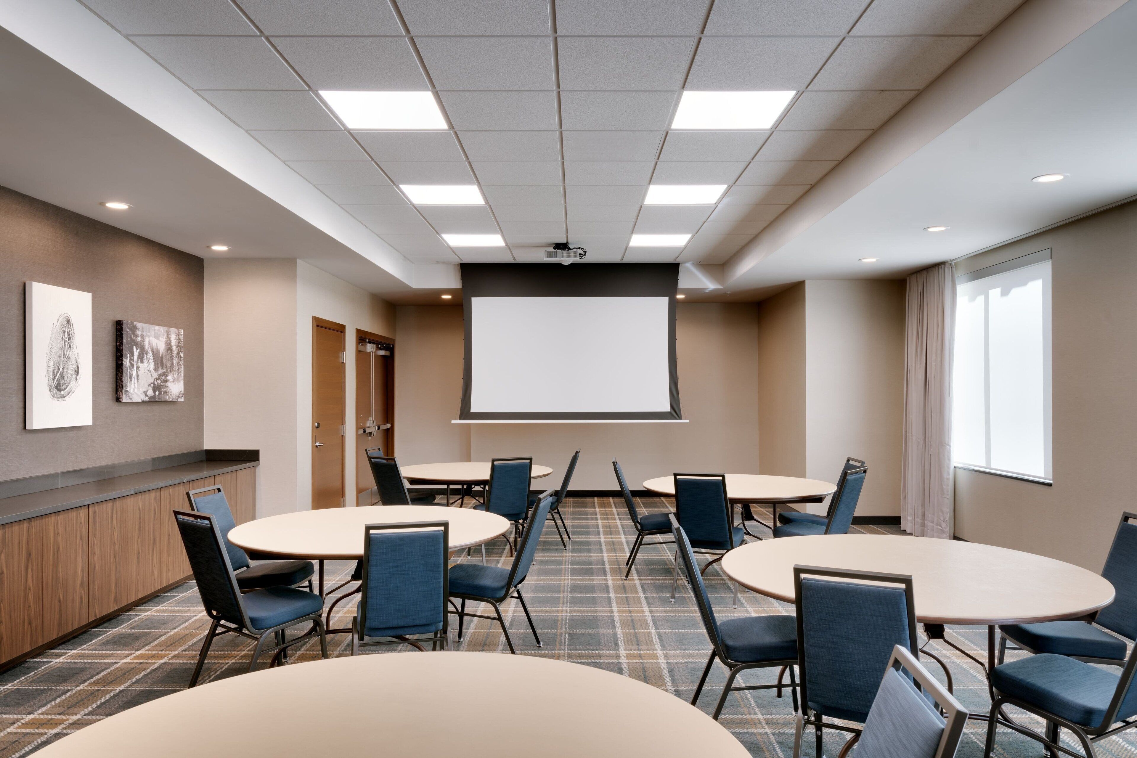 A conference room with a large screen, multiple tables, and chairs.
