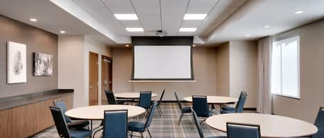 A conference room with a large screen, multiple tables, and chairs.