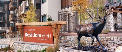 A sign for the Vail Colorado Residence Inn by Marriott, featuring a deer statue and a stone wall with plants.