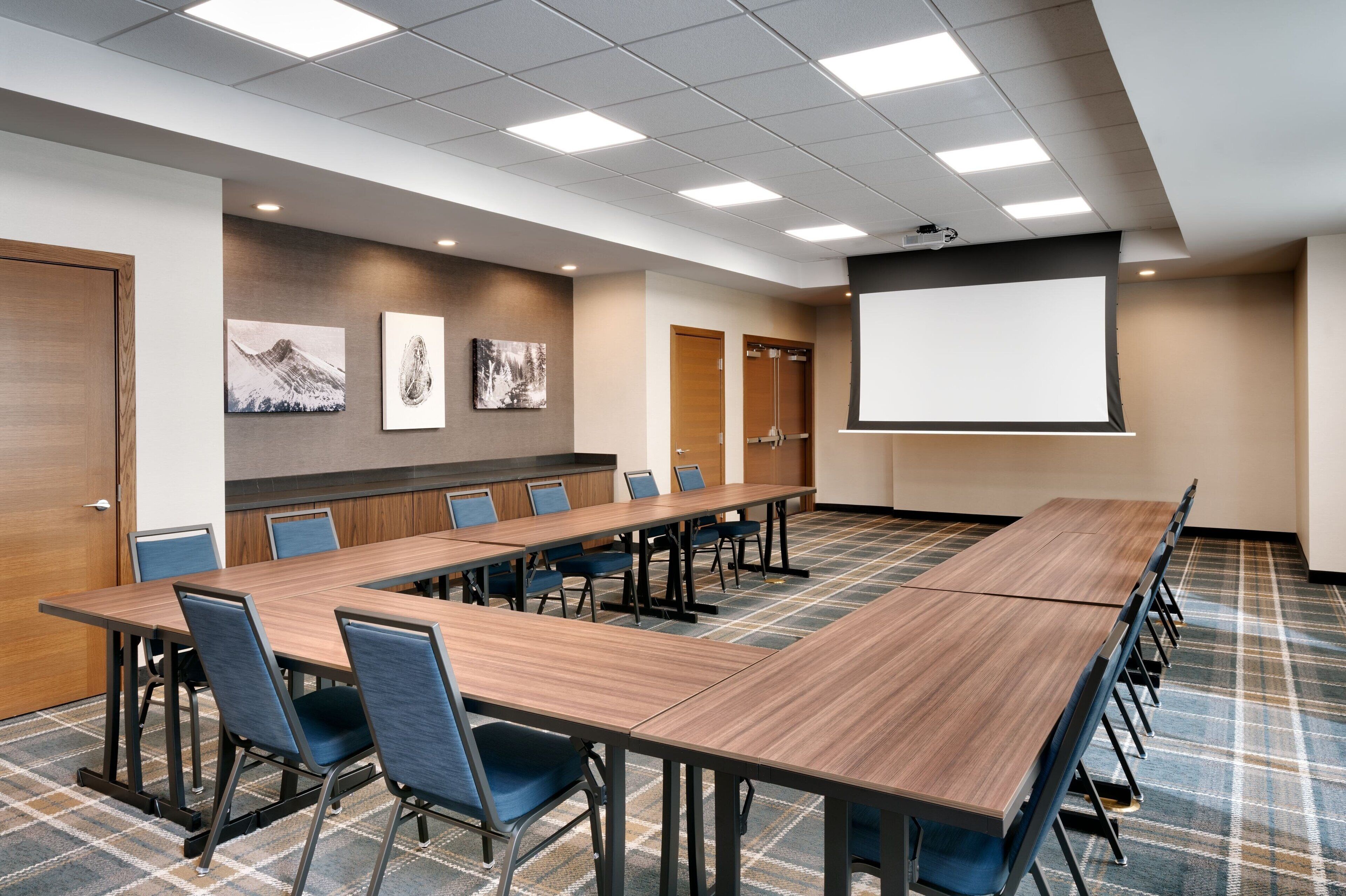 A conference room with a long table, chairs, a projector screen, and artwork on the walls.