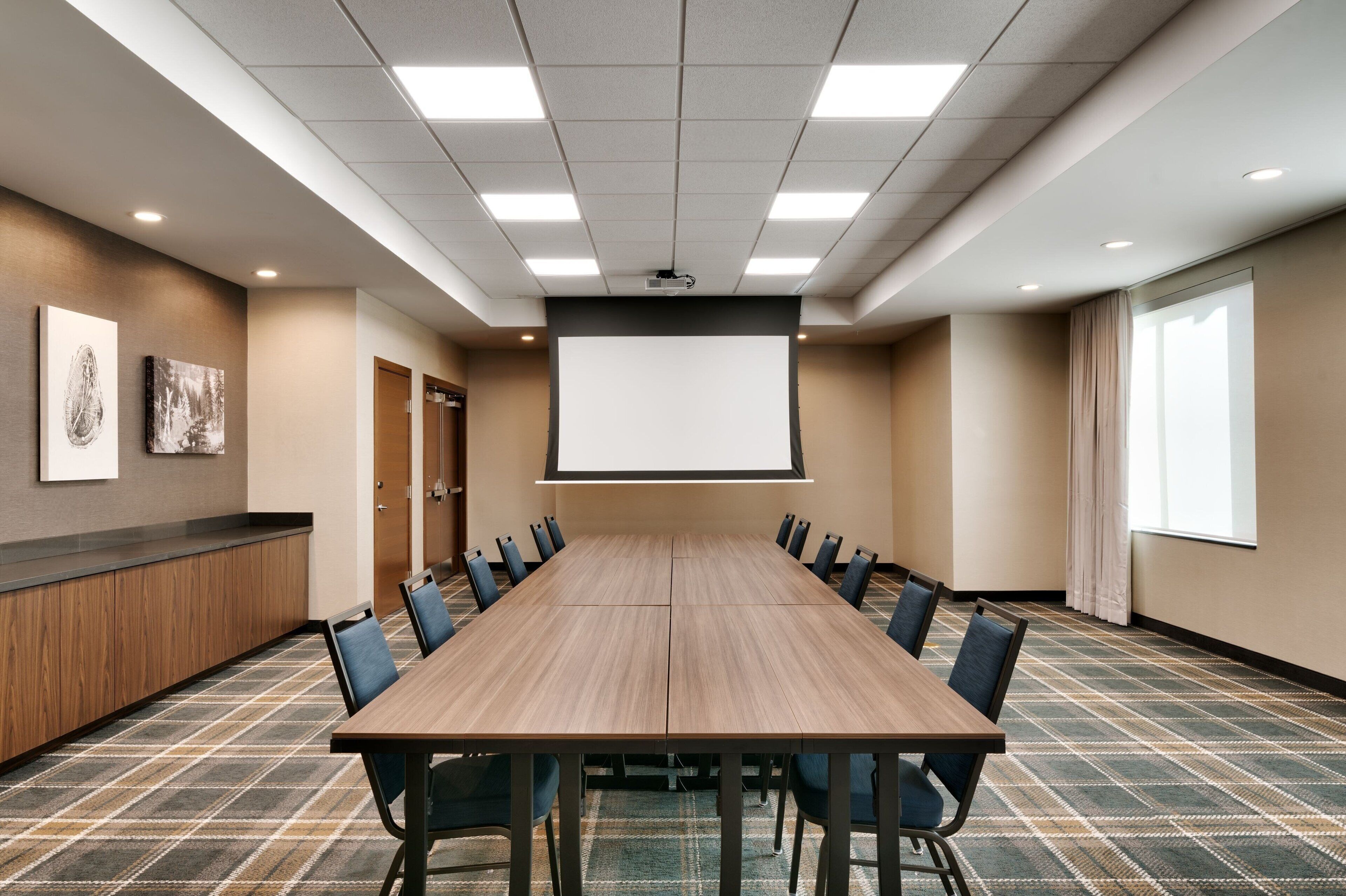A conference room with a long table, chairs, a projector screen, and a carpeted floor.