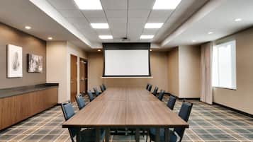 A conference room with a long table, chairs, a projector screen, and a carpeted floor.