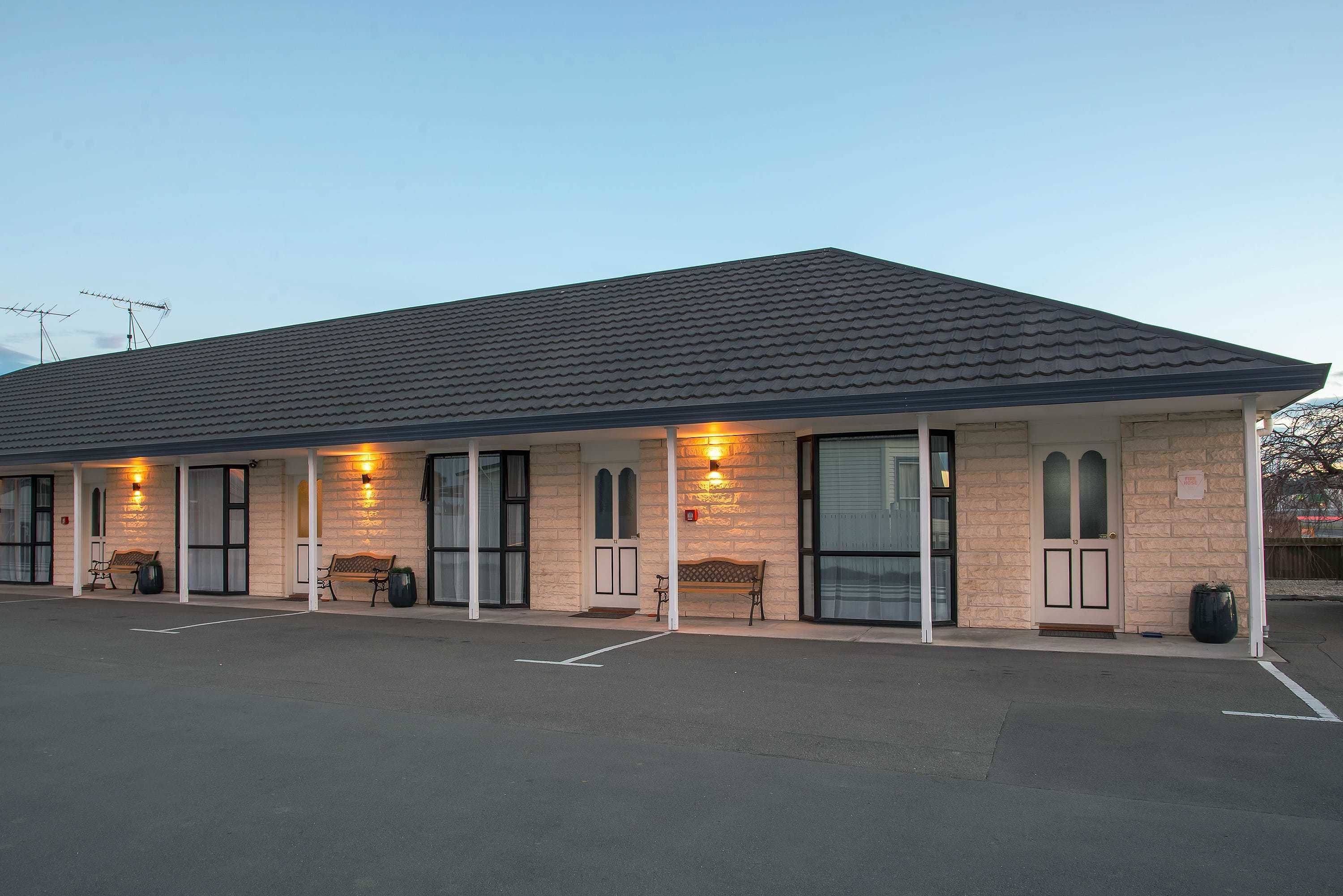 Un motel doté d’un parking couvert, de plusieurs chambres avec de grandes fenêtres et d’un espace extérieur aménagé pour s’asseoir.