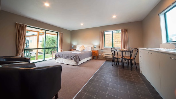 A bedroom with a large bed, a desk, and a chair, a bathroom, and a view of the outdoors. - Coronation Park (Ashburton)