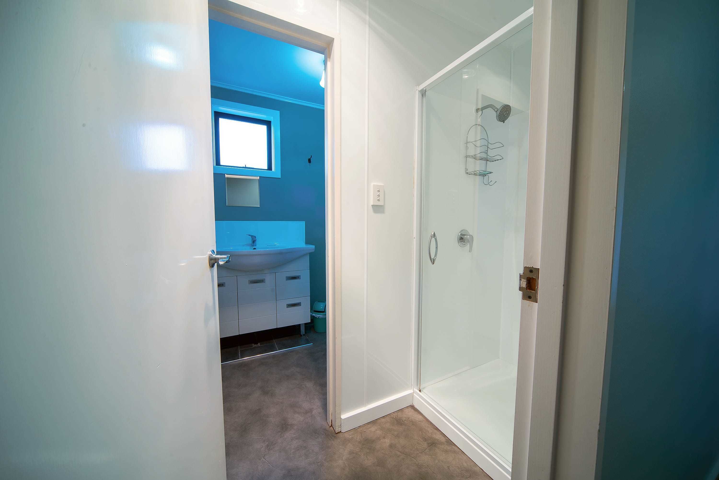 Un baño con mampara de vidrio, lavamanos y ventana sobre el espejo.