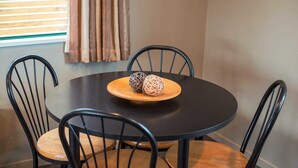 A round table with a dark surface and a wooden plate holding two decorative balls, surrounded by four black chairs with wooden seats. - Coronation Park (Ashburton)