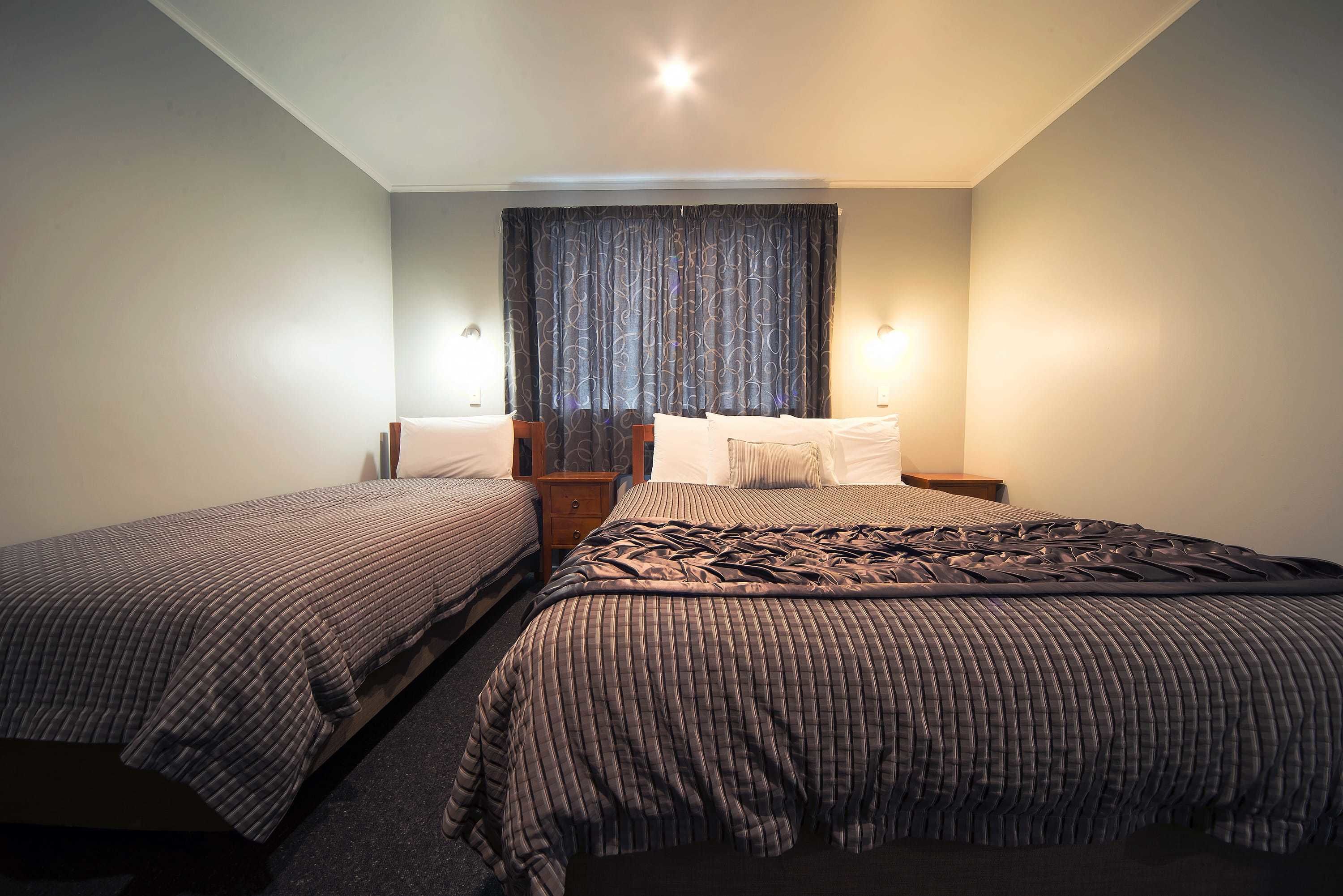 A hotel room with two single beds, a nightstand, a lamp, and a window with curtains.