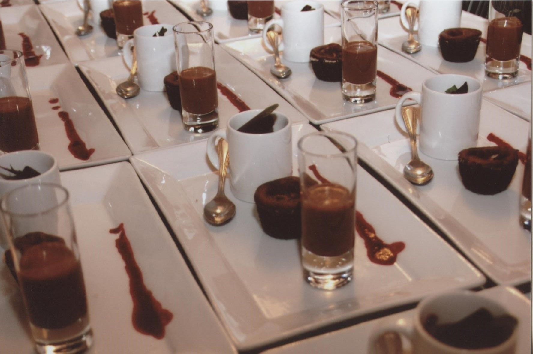 A table set with multiple plates of chocolate desserts, each accompanied by a spoon and a glass.