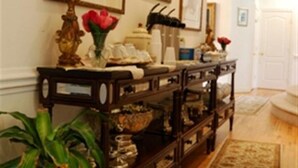 A hallway with a wooden floor, a console table with decorative items, framed artwork on the walls, and a door at the end. - The Columbia Inn at Peralynna Manor (Columbia)