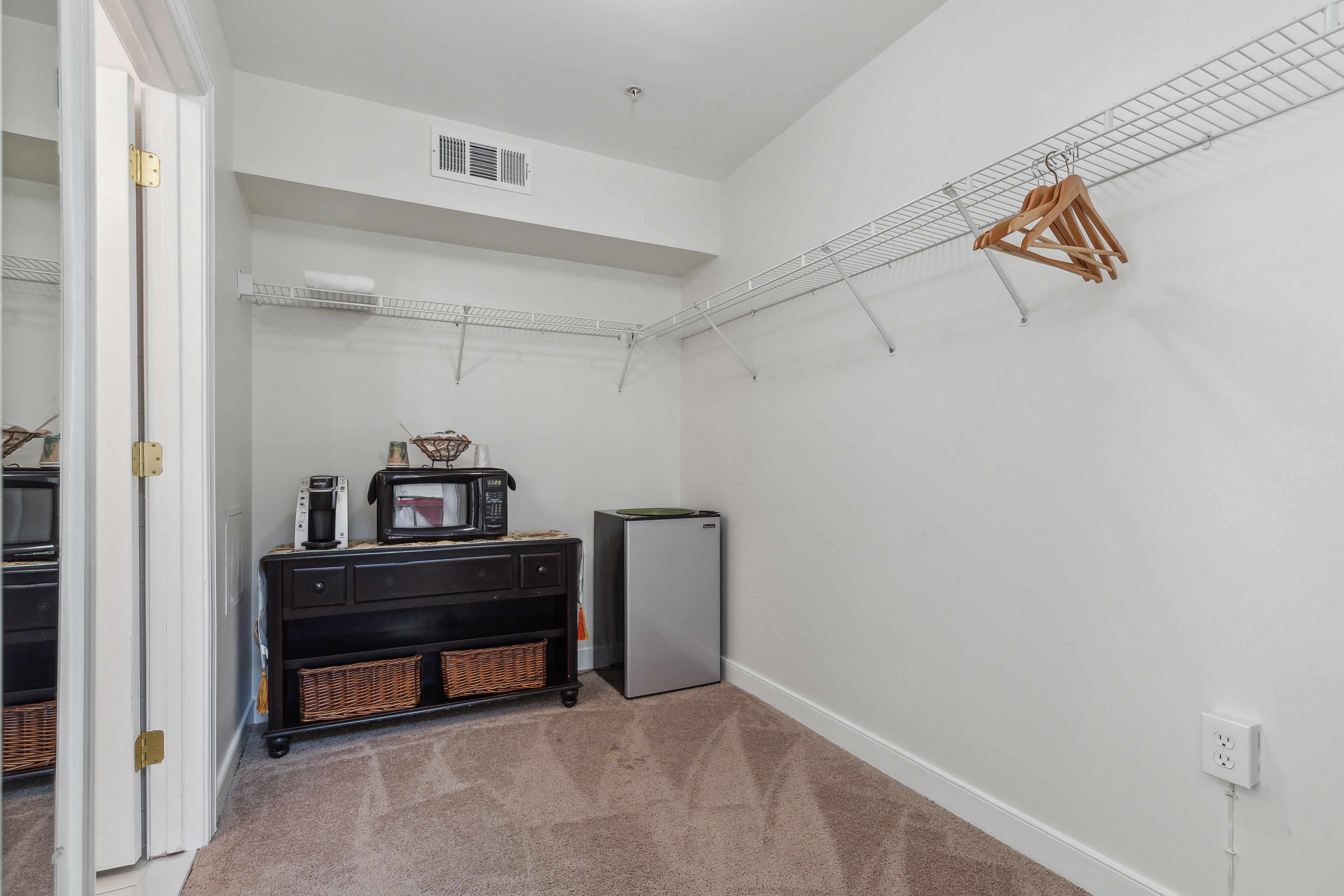 A compact kitchen with a microwave, refrigerator, and a small black cabinet with wicker baskets.