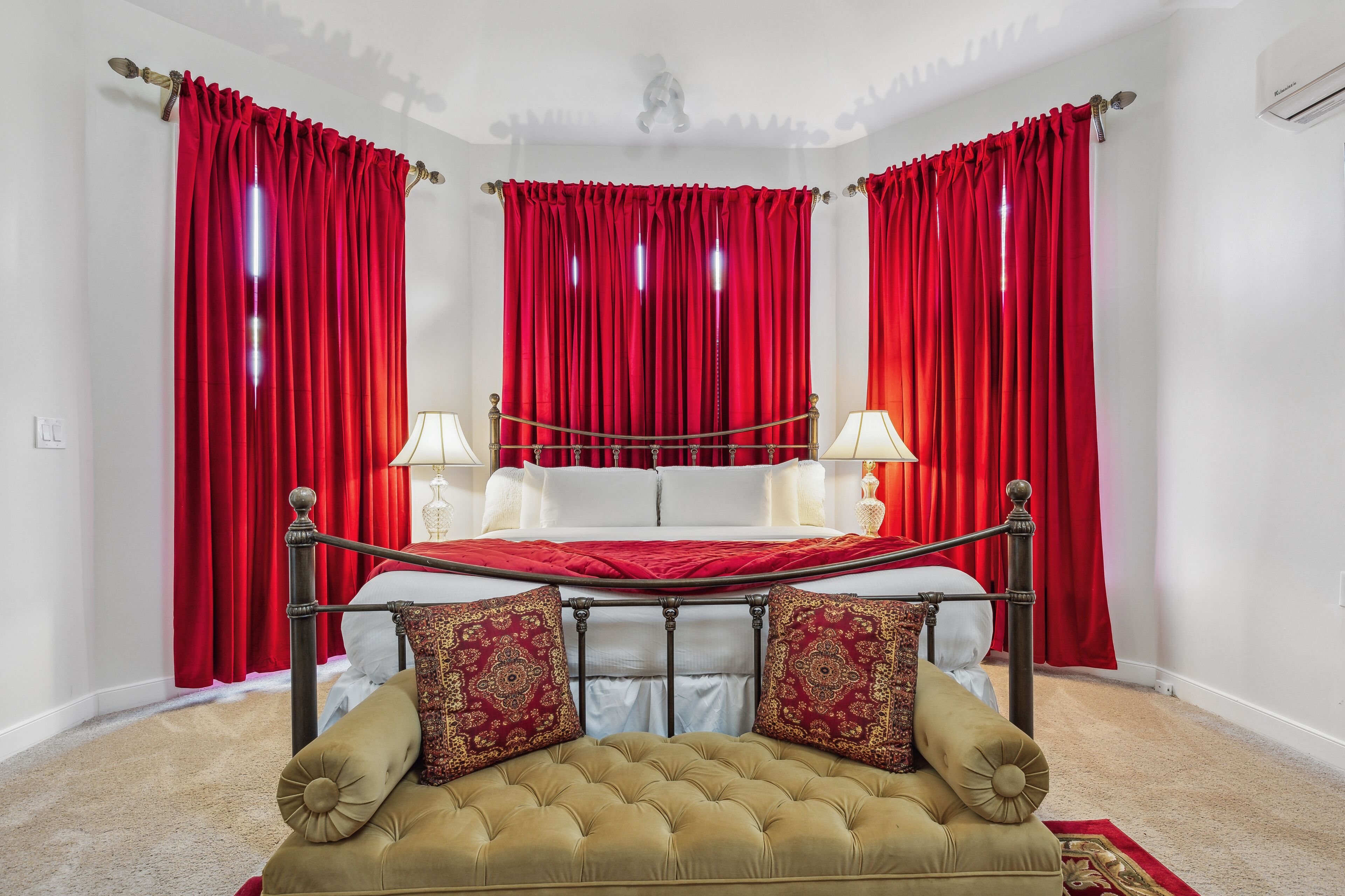 Un dormitorio con una cama con dosel, cortinas rojas, un sofá beige y dos lámparas de noche.