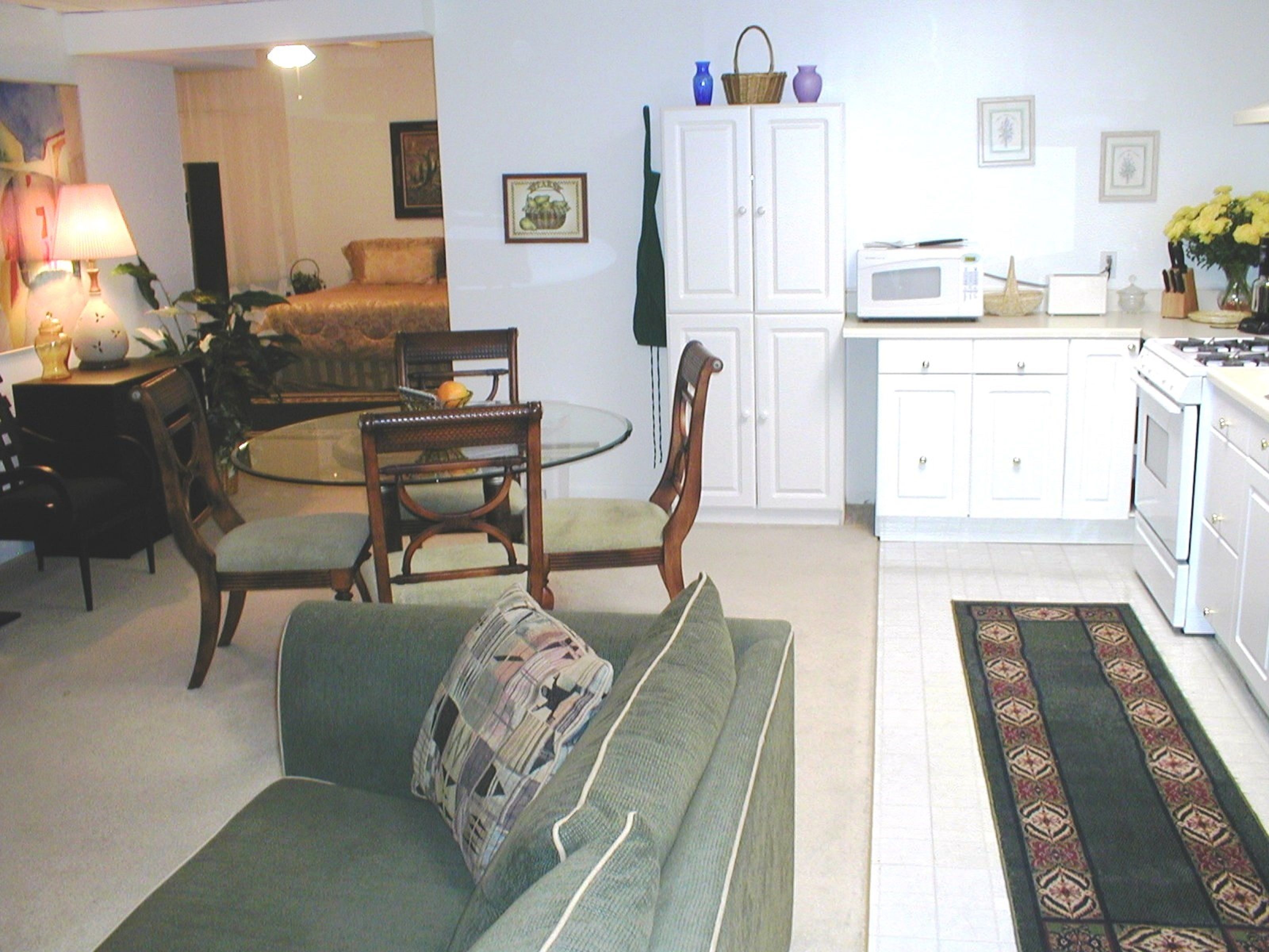 A living room with a green sofa, a dining table with chairs, a kitchen area with white cabinets, and a microwave.