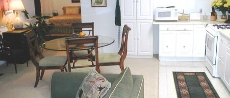 A living room with a green sofa, a dining table with chairs, a kitchen area with white cabinets, and a microwave.