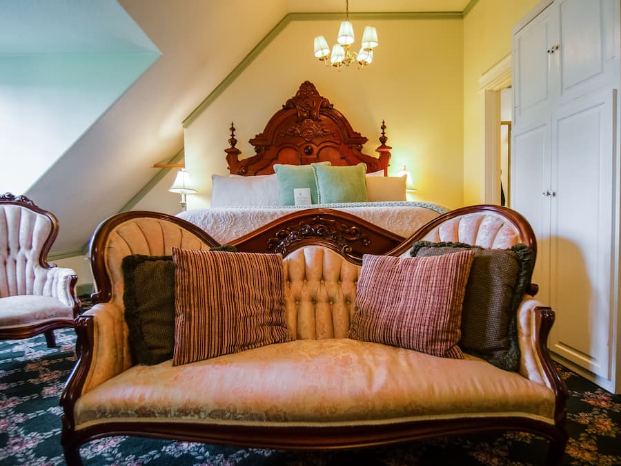 A bedroom with a large bed, a wooden headboard, a sitting area with a sofa, and a chandelier.