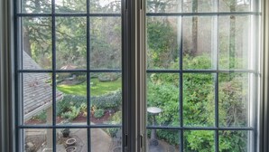 Vista a través de una ventana con diseño de celosía, mostrando un jardín con diversas plantas y árboles.