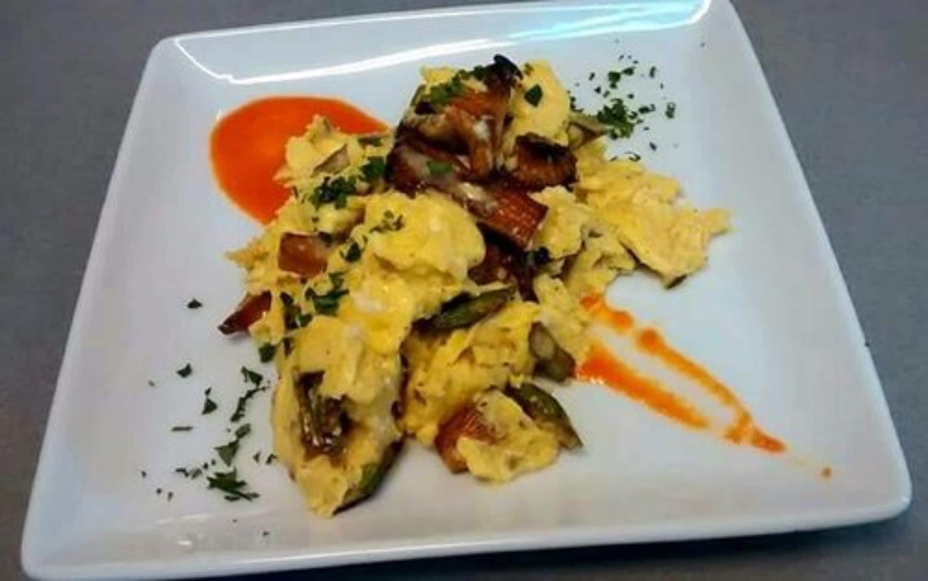 En firkantet hvid tallerken med røræg, grøntsager og rød sauce.