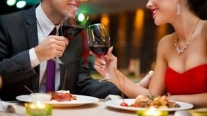 Una pareja brindando con copas de vino en una mesa de restaurante con platos de comida y velas.