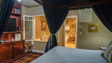 A bedroom with a canopy bed, a wooden dresser, a television, and a bathroom visible through an open door.