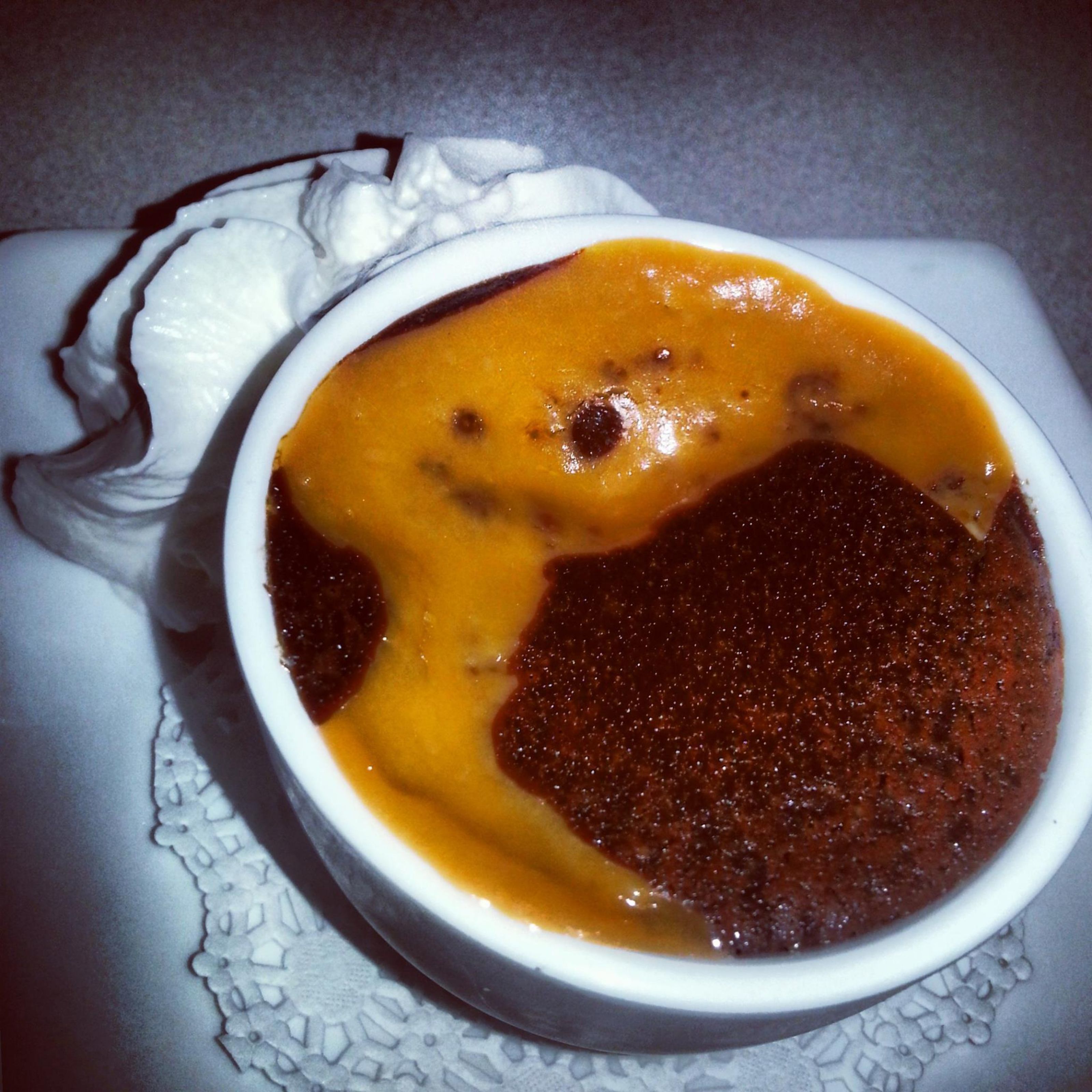 Un tazón de sopa con una capa superior cremosa y una base oscura, servido en un tazón blanco sobre un posavasos de encaje.