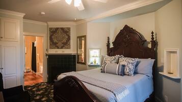 A bedroom with a wooden bed, a ceiling fan, a fireplace, and a hallway leading to another room.
