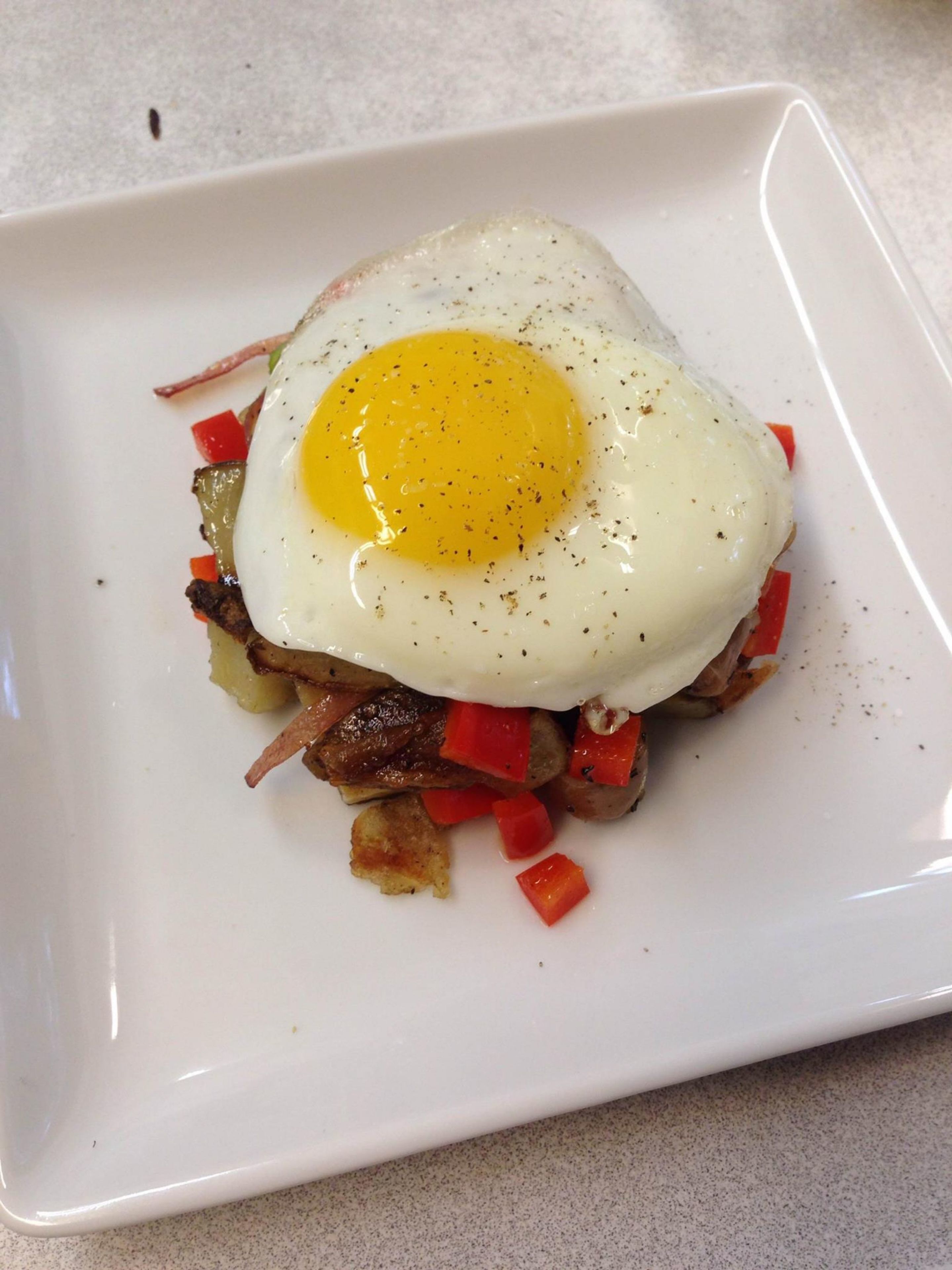 Un plato cuadrado blanco con un huevo frito sobre una guarnición de verduras y carne salteadas.