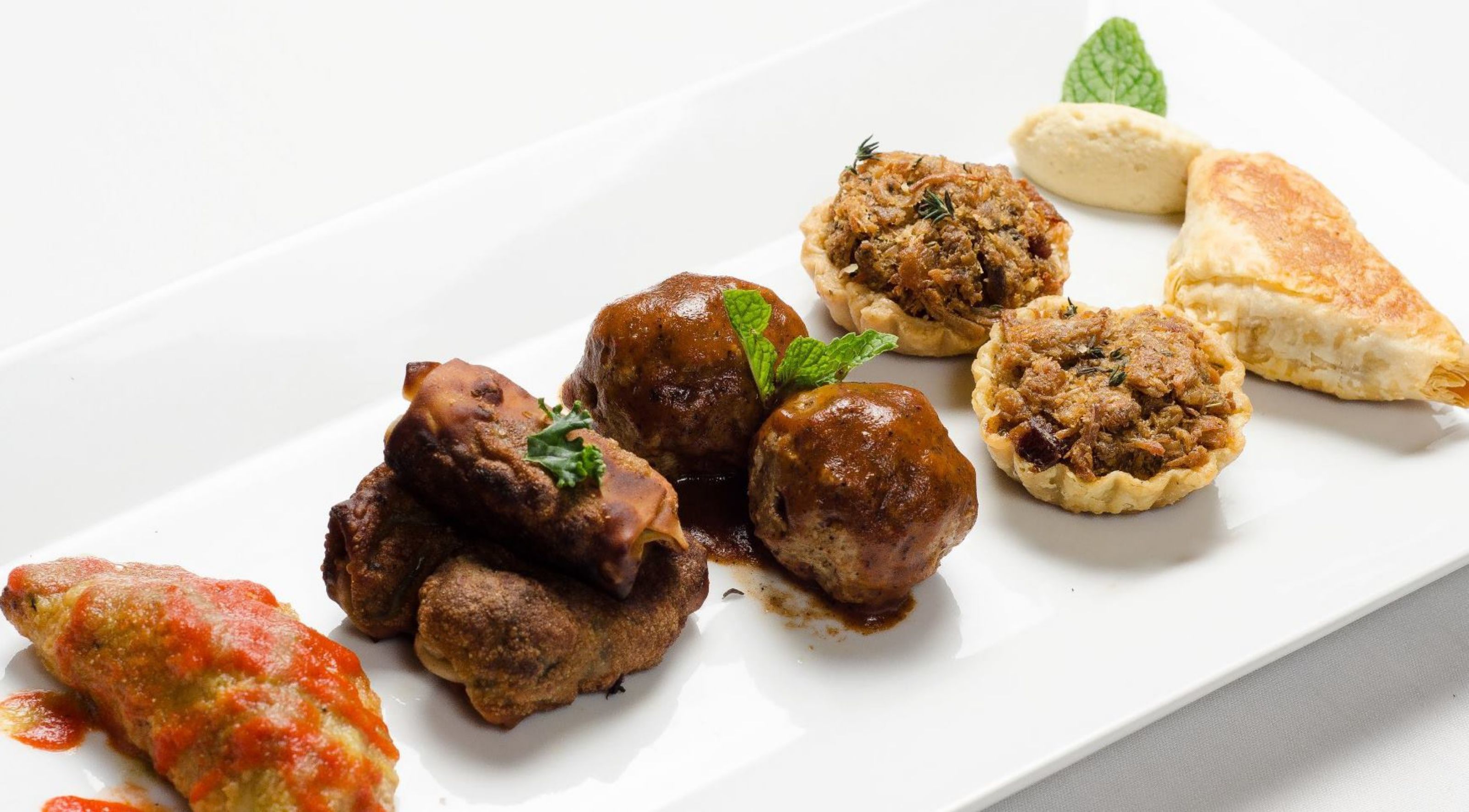 A variety of food items on a white plate, including meatballs, a pastry, and a stuffed bread.