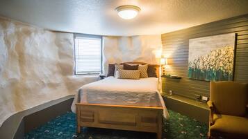 Un dormitorio con cama de madera, una mesita de noche con lámpara, una silla, una ventana con persianas y un cuadro colgado en la pared.