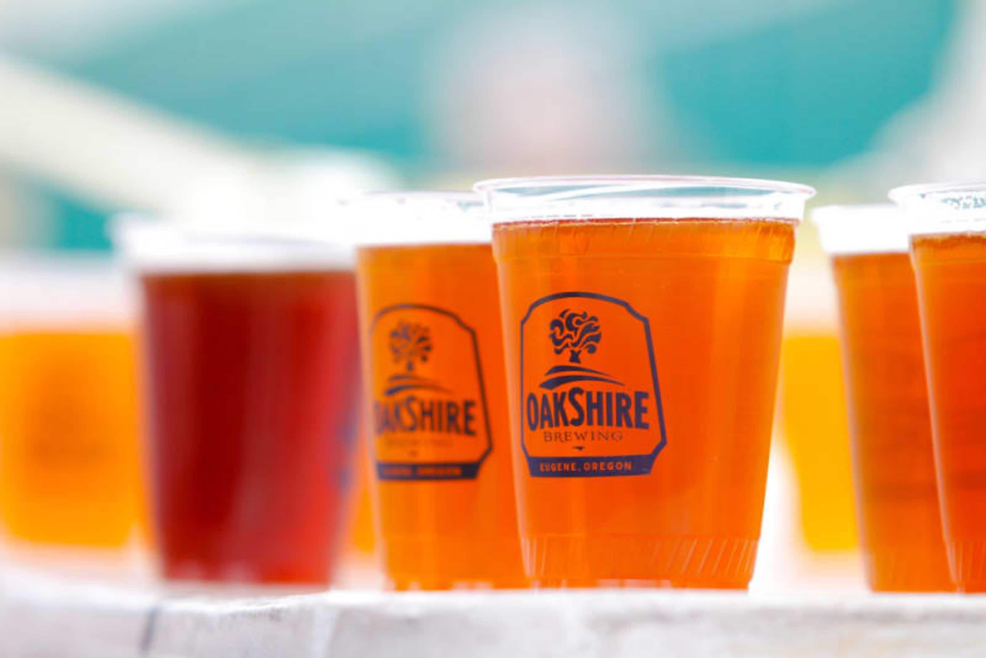 Una hilera de vasos de plástico con el logotipo de Oakshire Brewing, señal de servicio de bebidas.