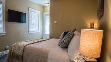 A bedroom with a bed, a lamp, a TV, and windows with blinds.