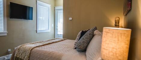 A bedroom with a bed, a lamp, a TV, and windows with blinds.