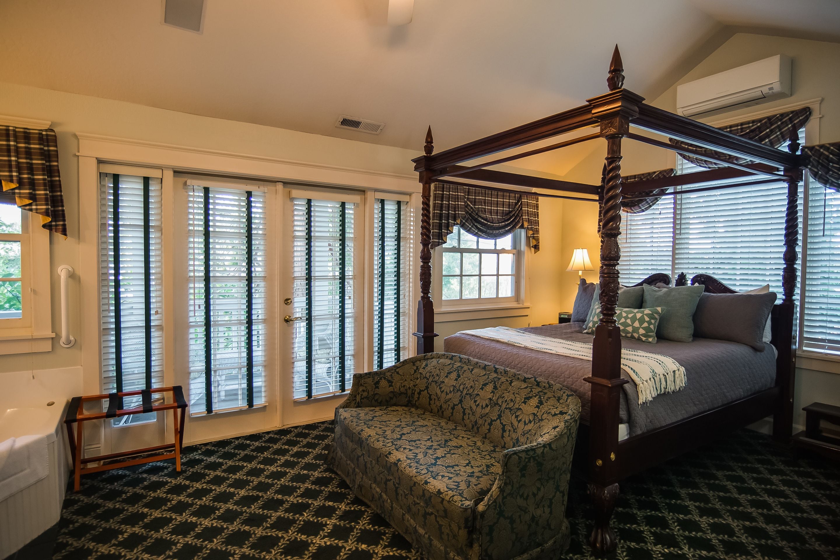 A bedroom with a four-poster bed, a chair, and a large window with blinds.