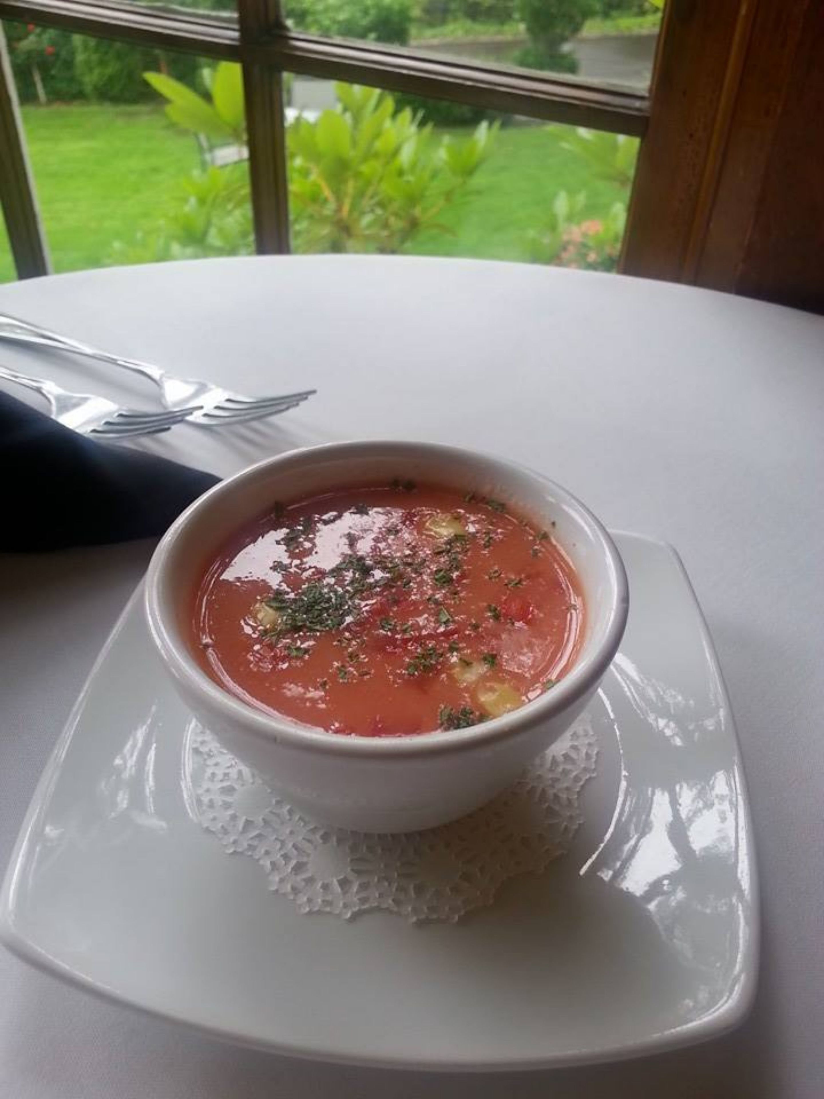 Un bol de sopa sobre un plat blanc, amb una petita tela de puntada al davall, damunt d'un taulell blanc.