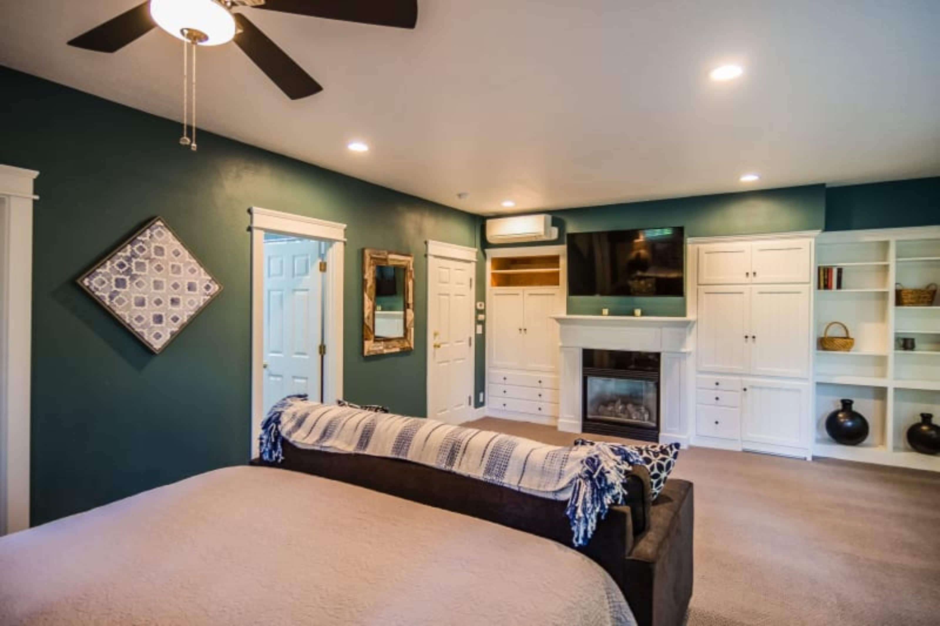 A bedroom with a bed, a ceiling fan, a fireplace, and built-in storage cabinets.
