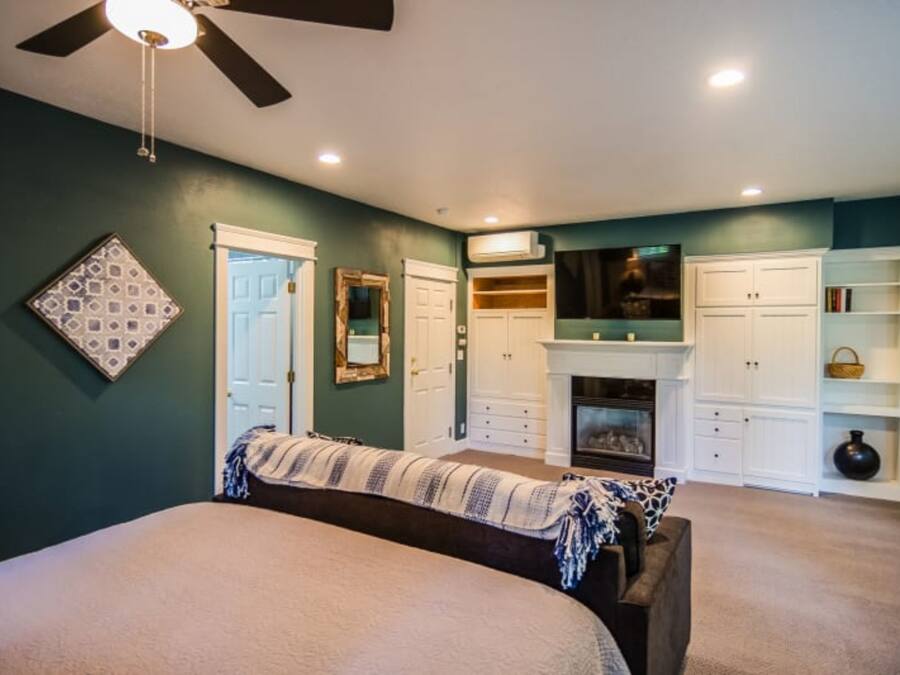 A bedroom with a bed, a ceiling fan, a fireplace, and built-in storage cabinets.