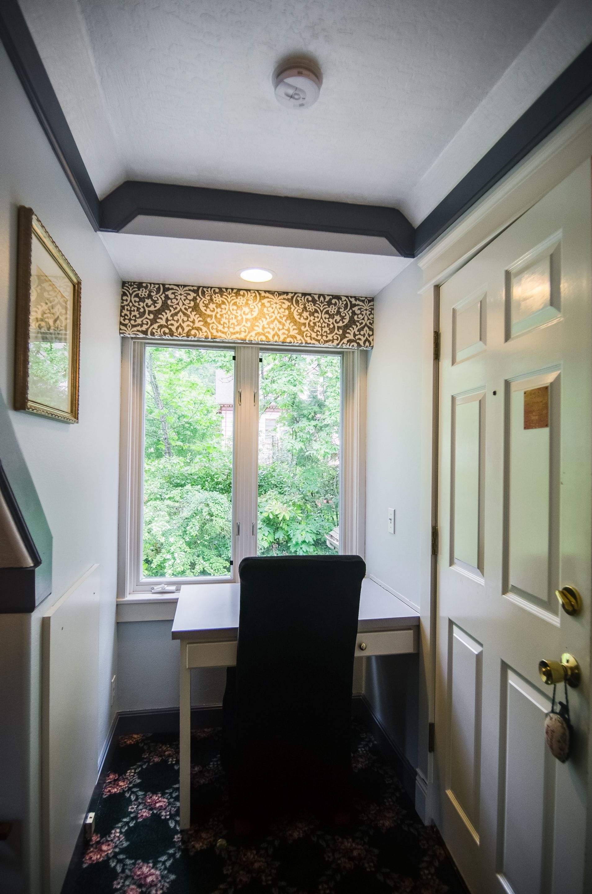 A corner room with a desk, chair, and a window with a view of greenery.
