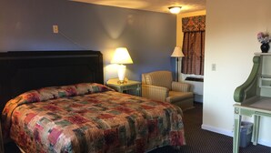 A hotel room with a large bed, a chair, a desk, and a lamp. - Budget Inn North Stonington (North Stonington)