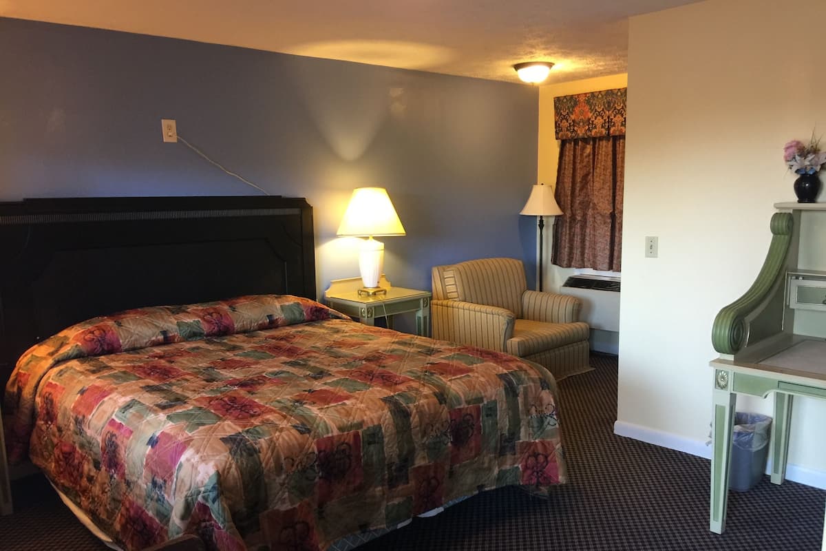A hotel room with a large bed, a chair, a desk, and a lamp.