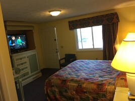 Habitación de hotel con cama, televisor, escritorio y ventana con cortinas.