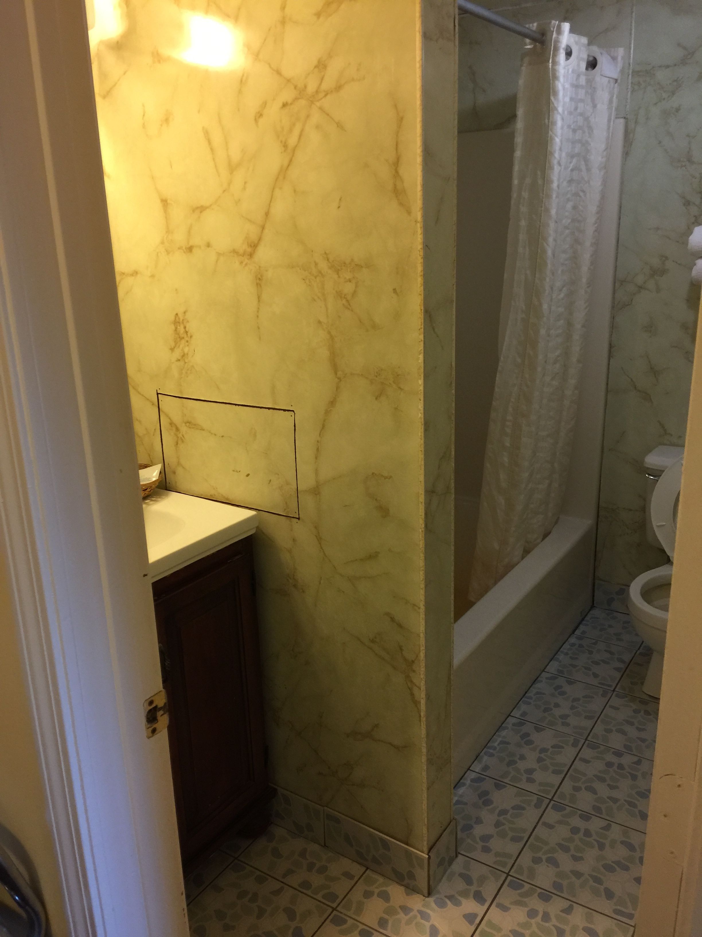 A bathroom with a marble wall, a shower with a curtain, a toilet, and a sink with a mirror.