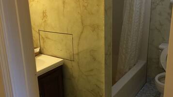 A bathroom with a marble wall, a shower with a curtain, a toilet, and a sink with a mirror.