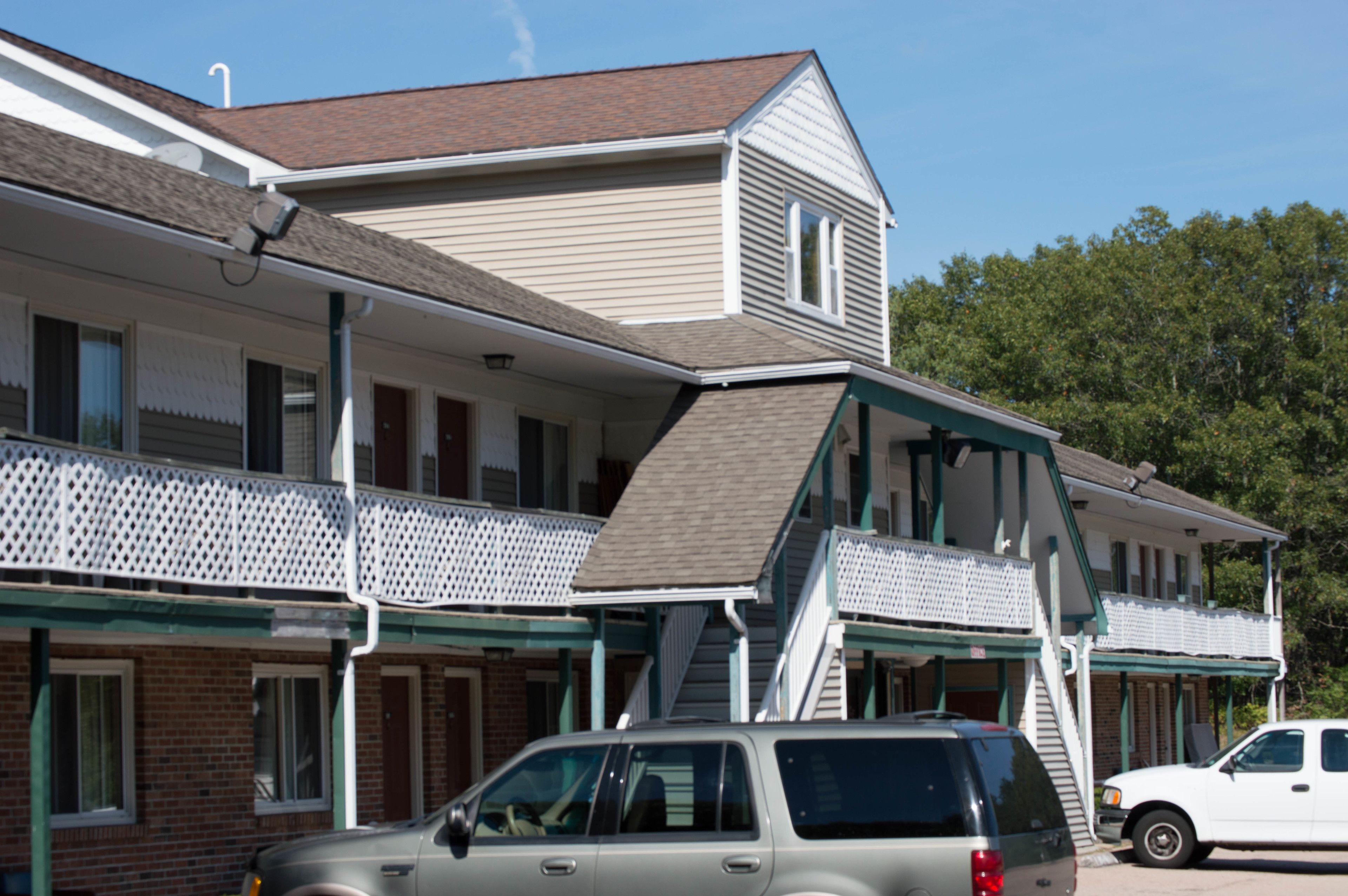 A two-story motel with a covered front porch, a staircase to the upper level, and a parking area with two vehicles.