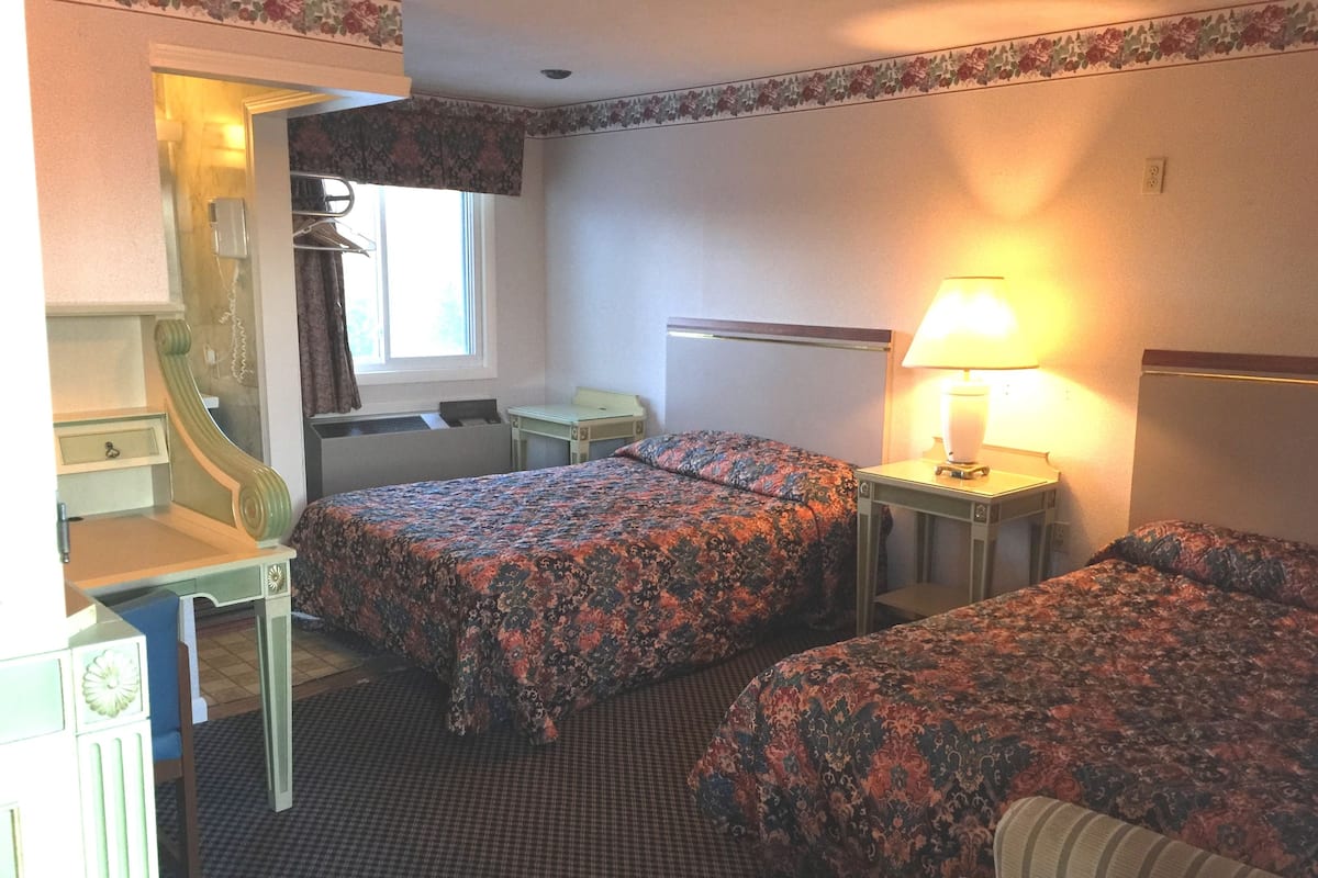 A hotel room with two beds, a desk, a chair, a lamp, and a mirror.