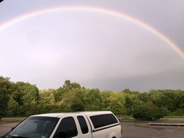 A white van parked in a lot with a rainbow in the background.