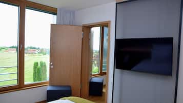 A bedroom with a large window, a bed, a TV mounted on the wall, and a wooden wardrobe.