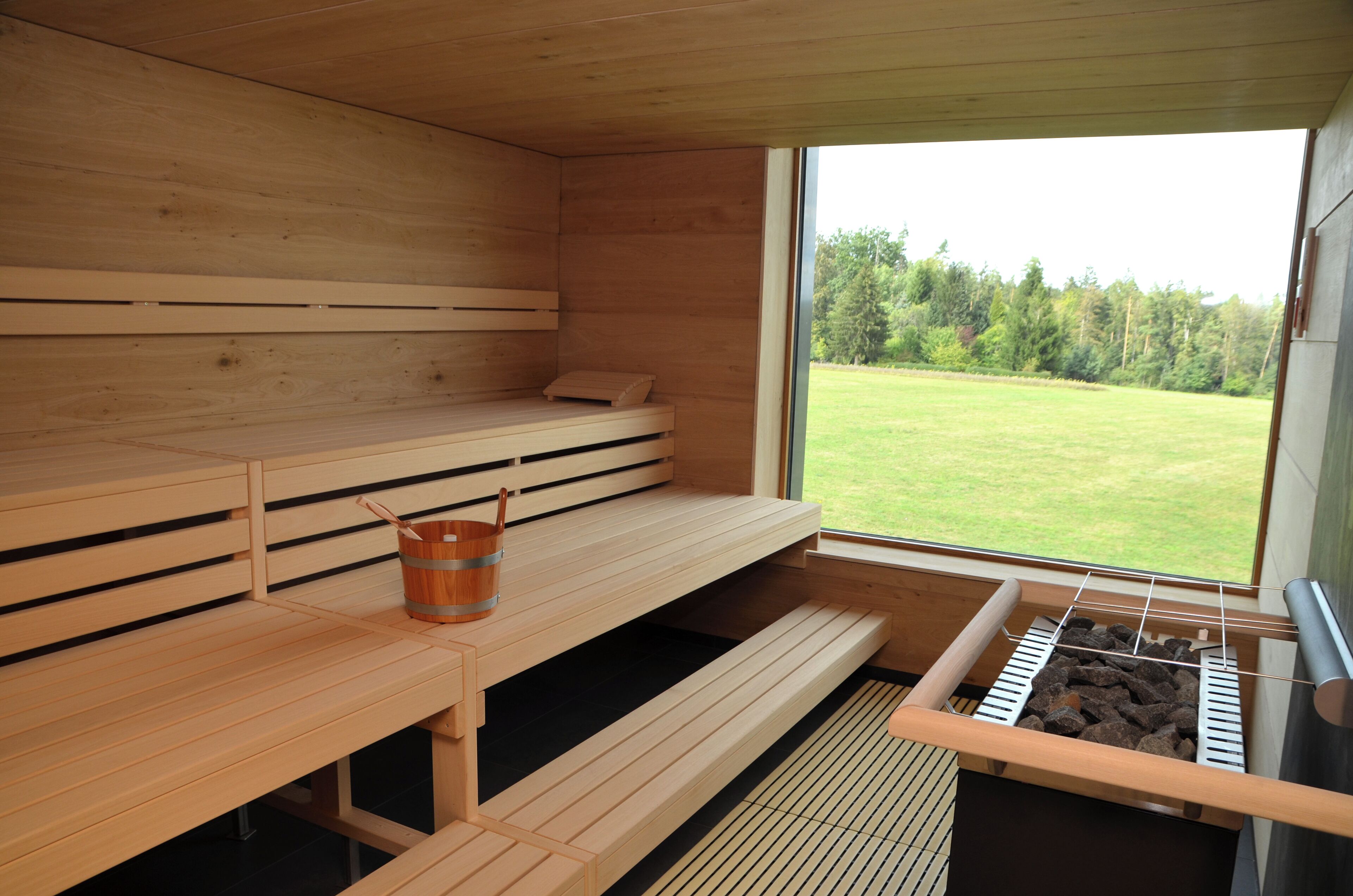 A sauna room with wooden benches, a bucket, and a sauna heater.