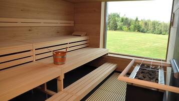 A sauna room with wooden benches, a bucket, and a sauna heater.